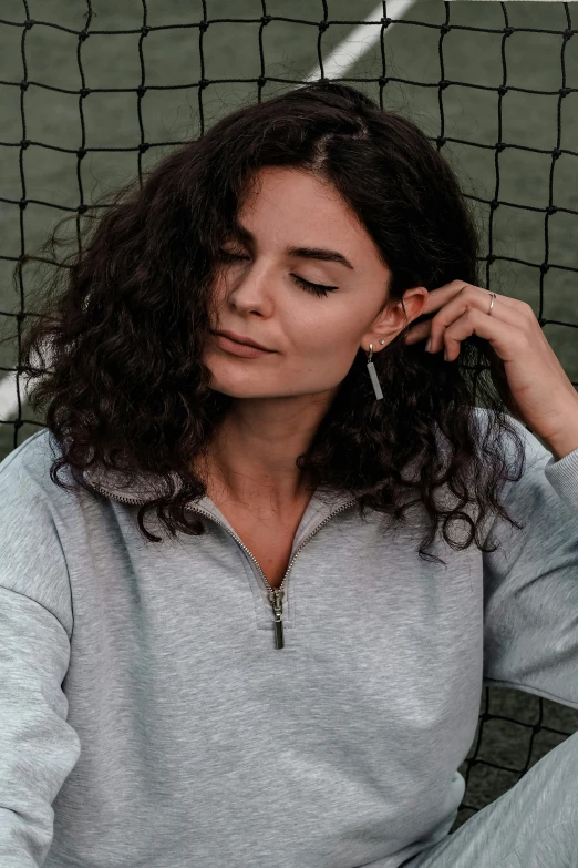 a woman sitting in front of a tennis net with her hand to her ear