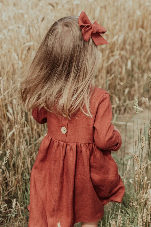 a girl in a red dress walks through a field