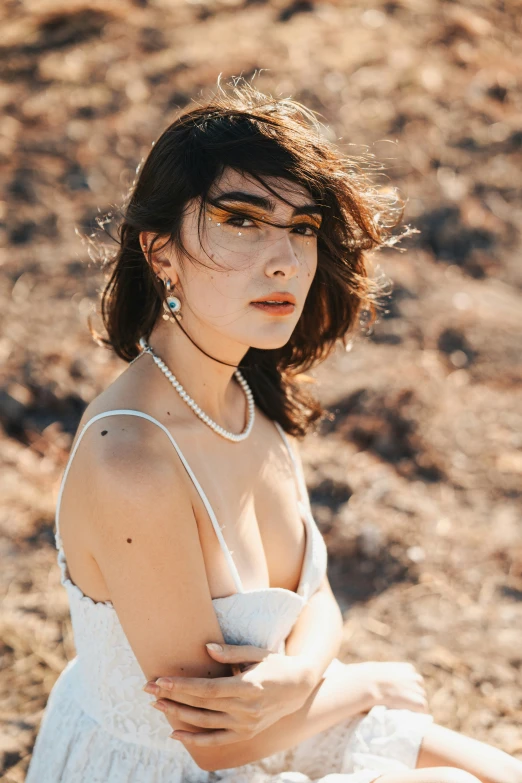 a woman with makeup is wearing pearls and sitting on the ground