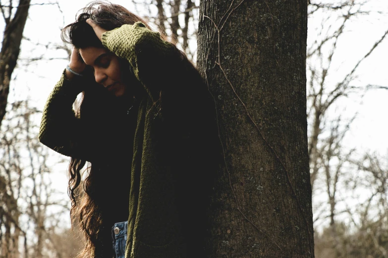 the woman in the black jacket stands next to a tree and looks into her ear