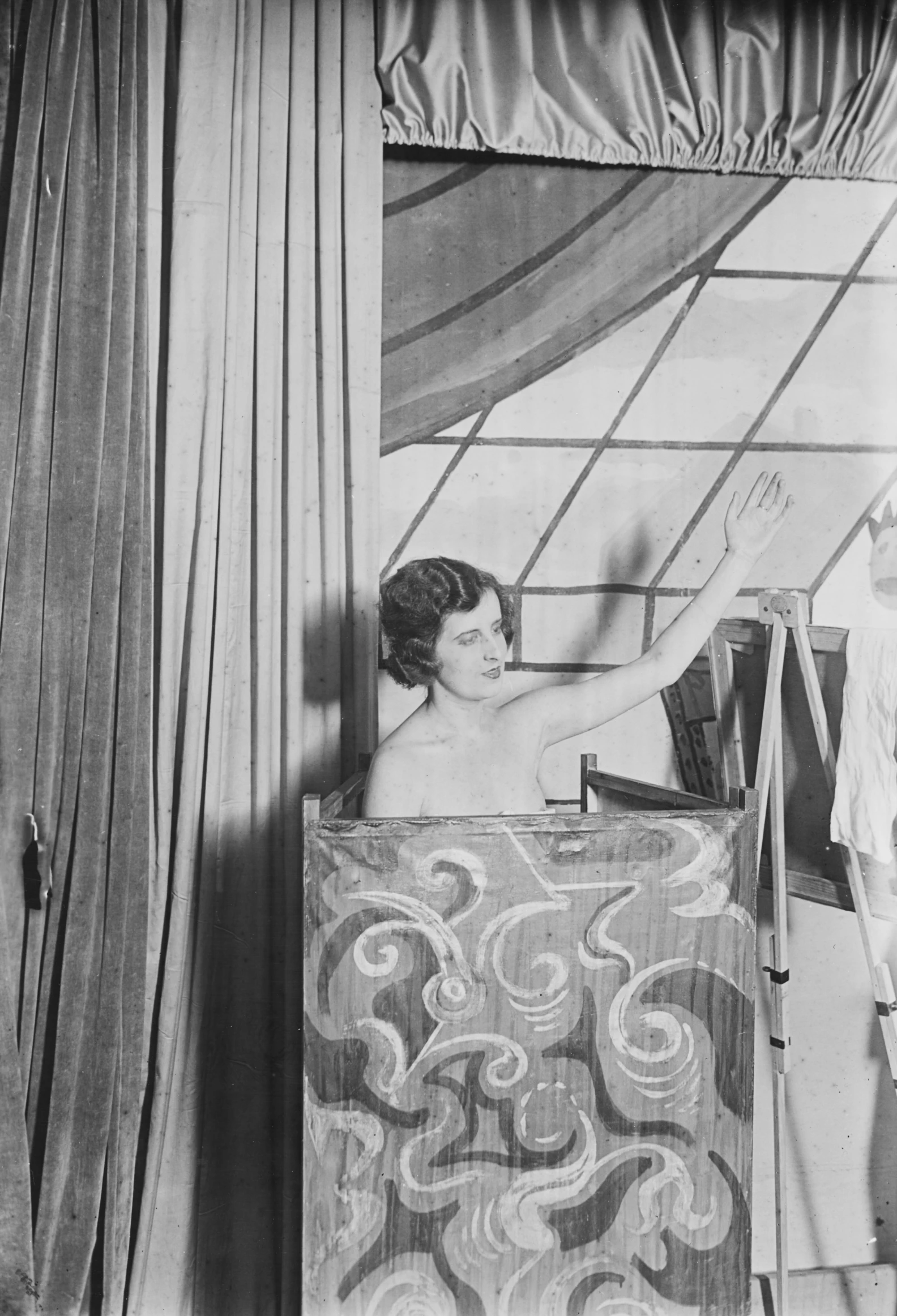 a woman standing in front of a curtain with her arm out and hand up