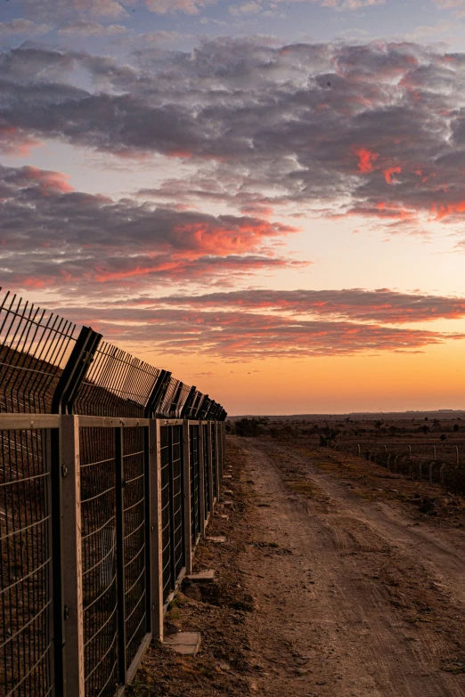 a dirt road next to a fence and field