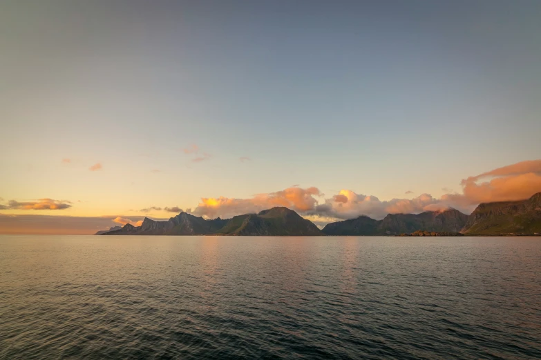 several mountains are seen from the ocean as the sun sets