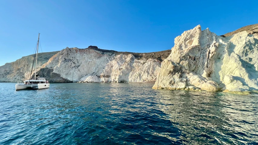 a sailboat sailing past an island on clear blue water