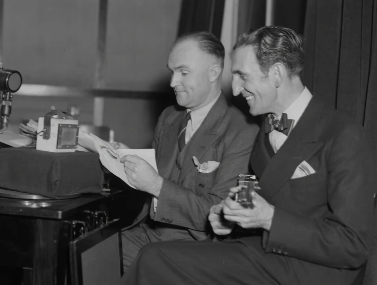 two men dressed in suits holding drinks and looking at papers