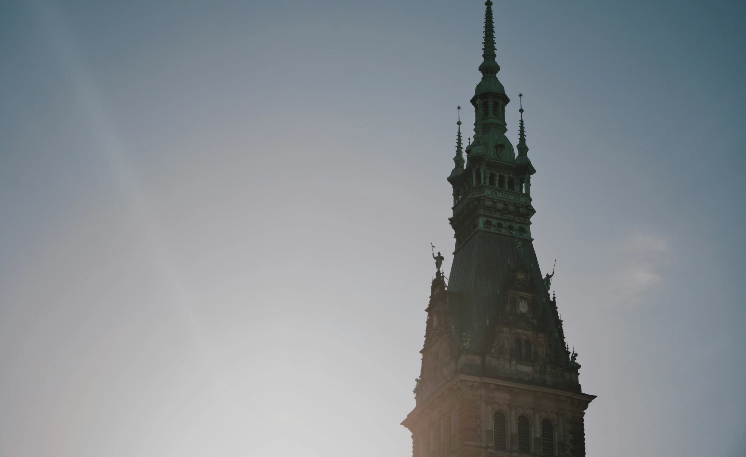 large clock tower against the grey sky with light reflection