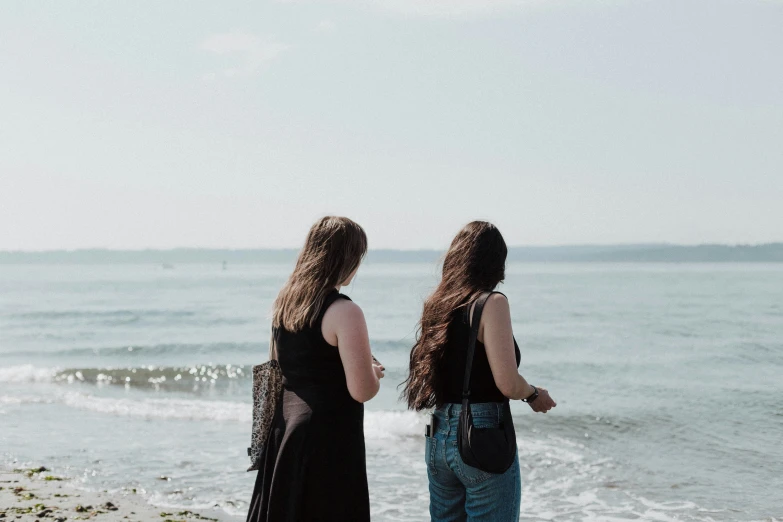 two girls stand facing the ocean looking out