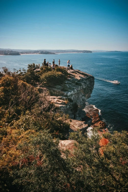 several people are standing on the edge of a cliff by a body of water