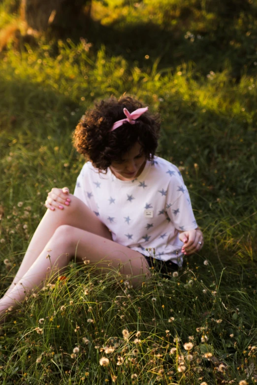 a girl sitting in the grass and holding her hand over her knees