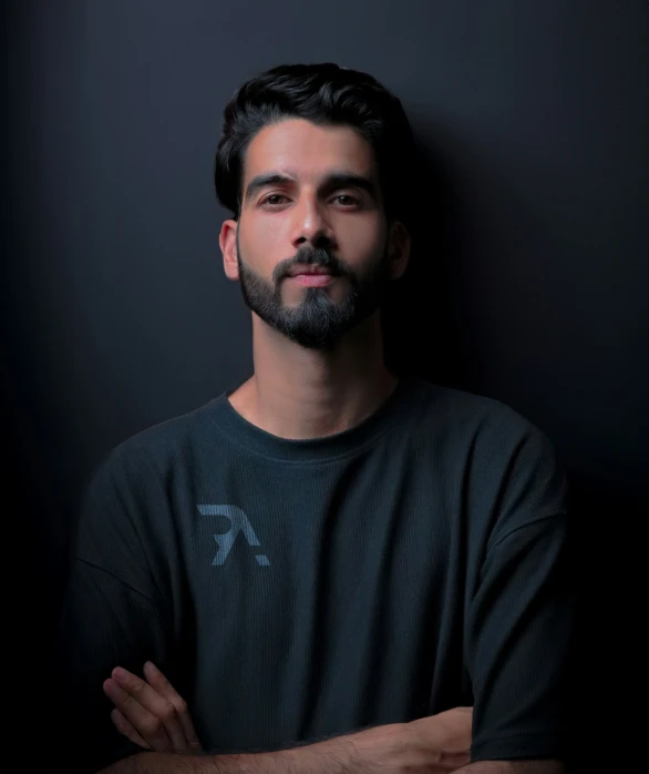 a man with a beard standing in front of a dark wall