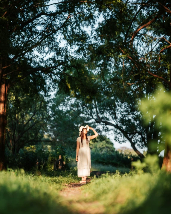 a woman in a white dress walks down a path under trees