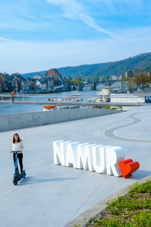 a girl standing in front of namur sign with water and buildings in background