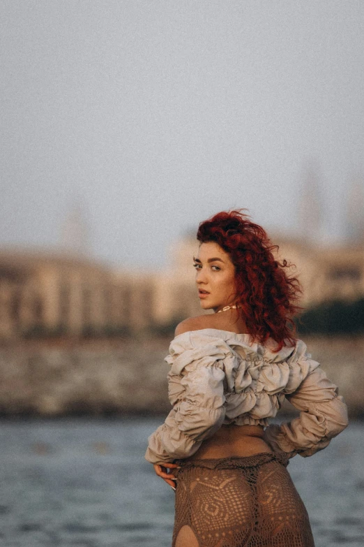 a woman with red hair is standing near water