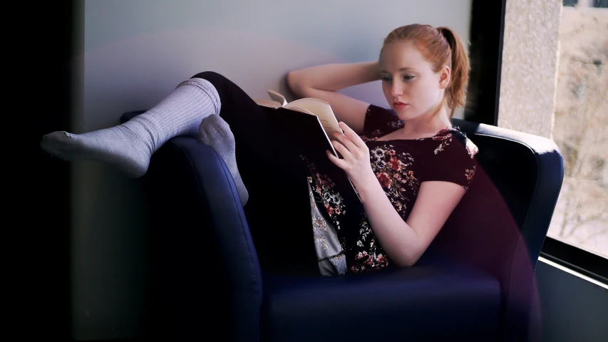 woman sitting on couch while reading book at daytime