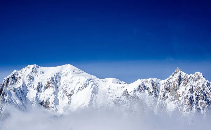 snow covered mountains stand below the clouds in the blue sky