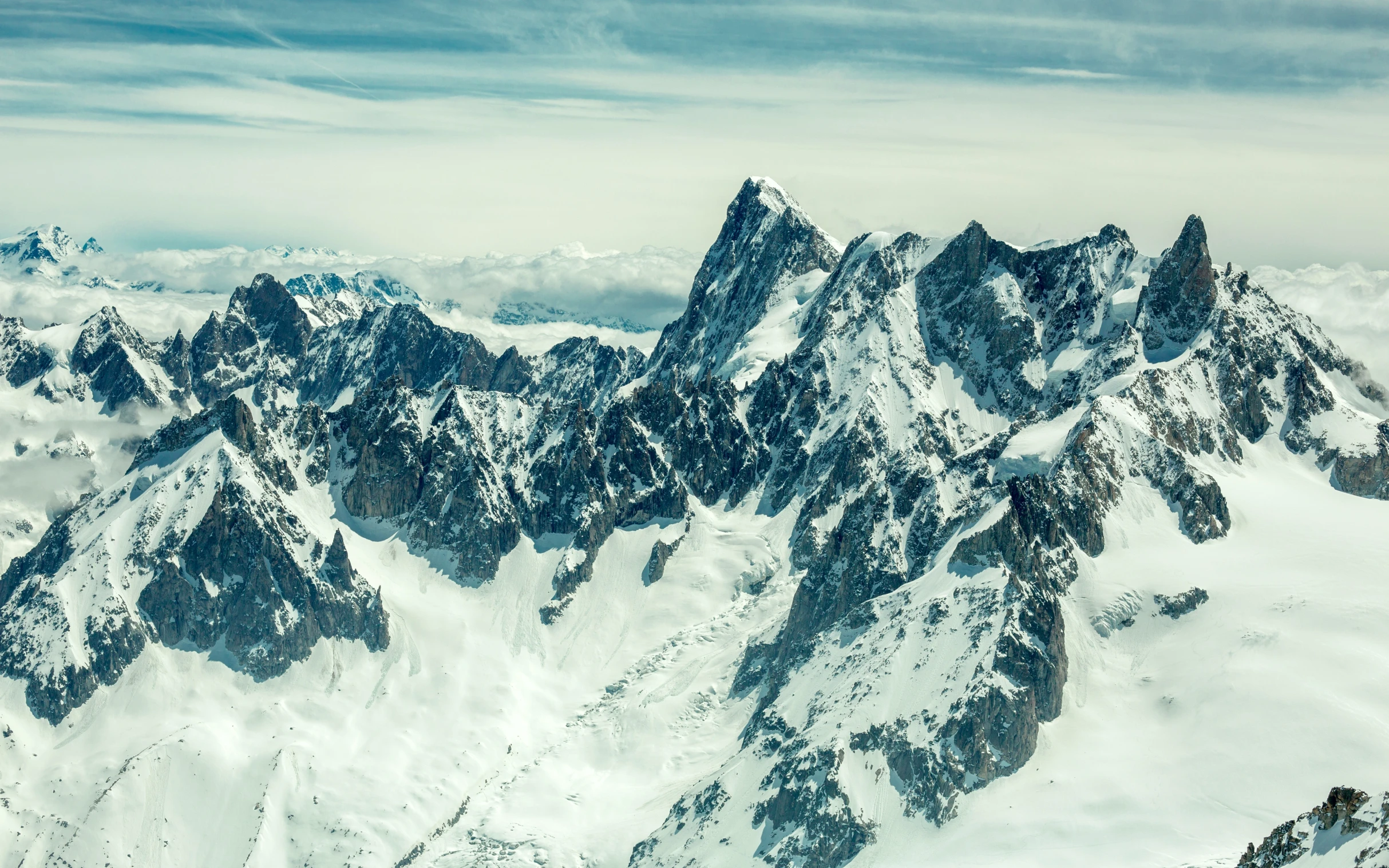 some mountains covered with snow and clouds under a blue sky