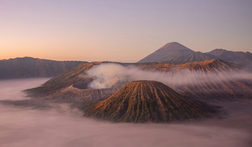 the smoke plumes from two mountain peaks as the sun goes down