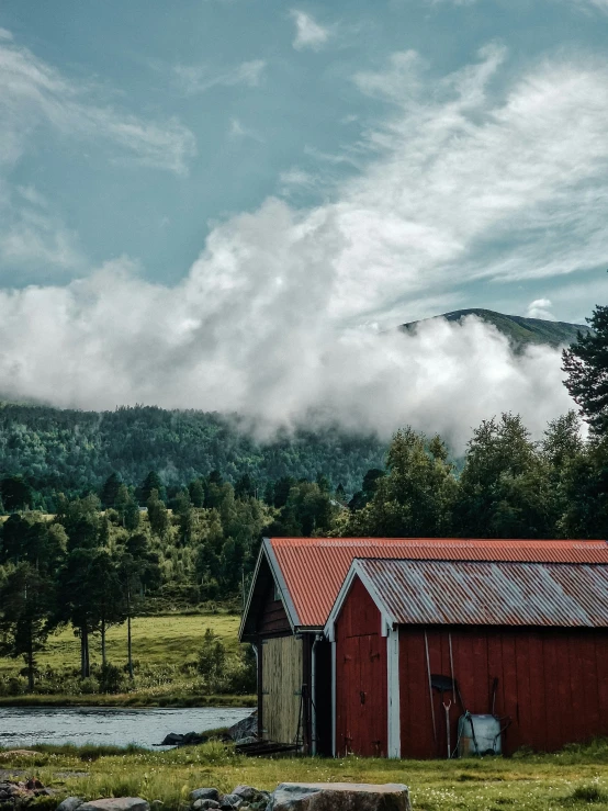 red barn on a grassy field with trees and mountains in the background