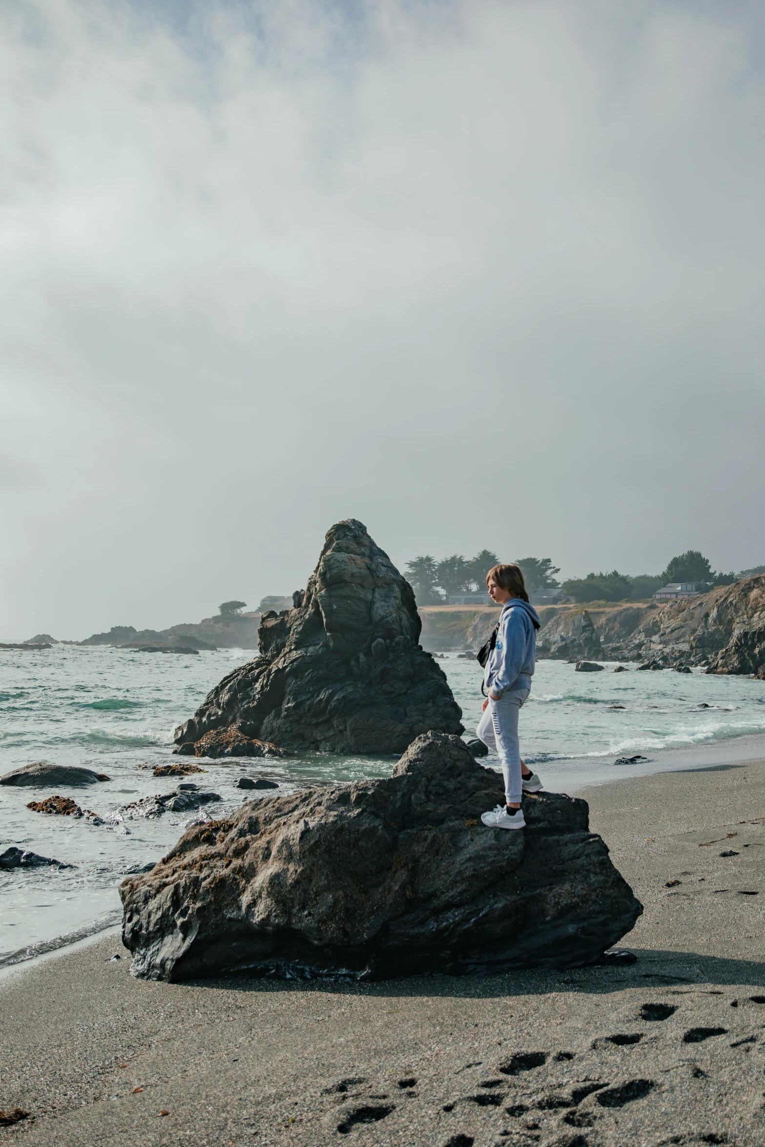 a woman standing on top of a rock next to a sandy beach