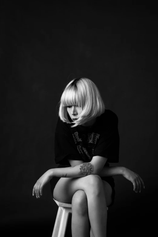 a woman sitting on top of a stool next to a black wall