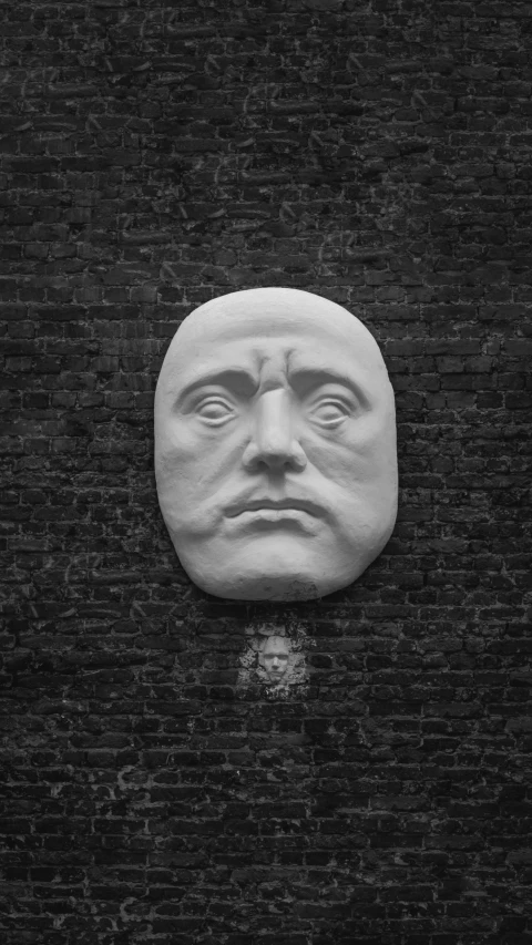 black and white image of a large face against a brick wall