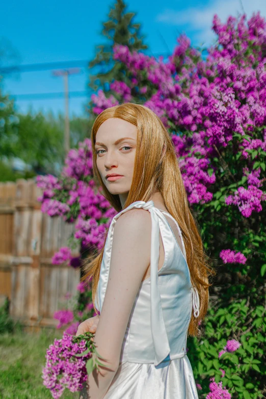 a girl wearing a white dress standing next to purple flowers