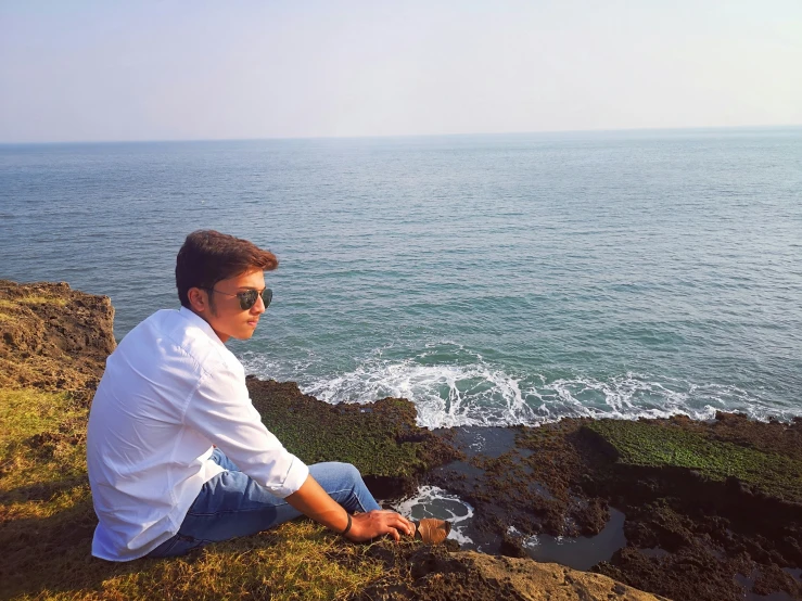 a man sitting on top of a cliff over looking the ocean