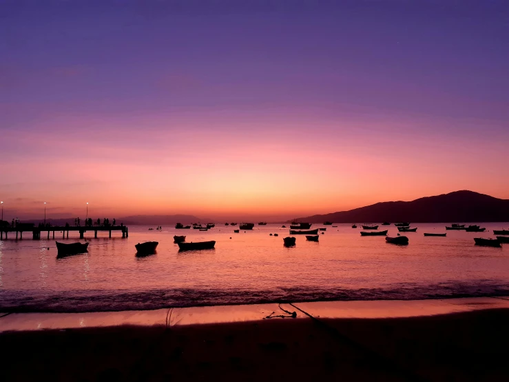 some boats are floating on the water as the sun sets