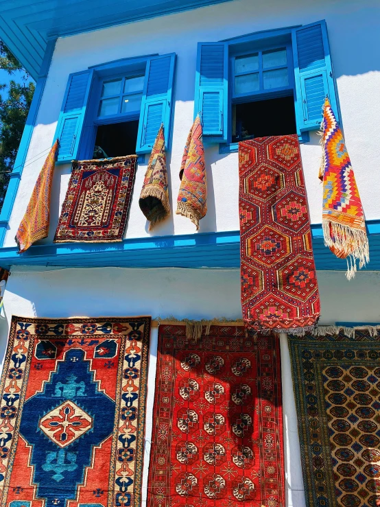 a number of rugs hanging near blue windows