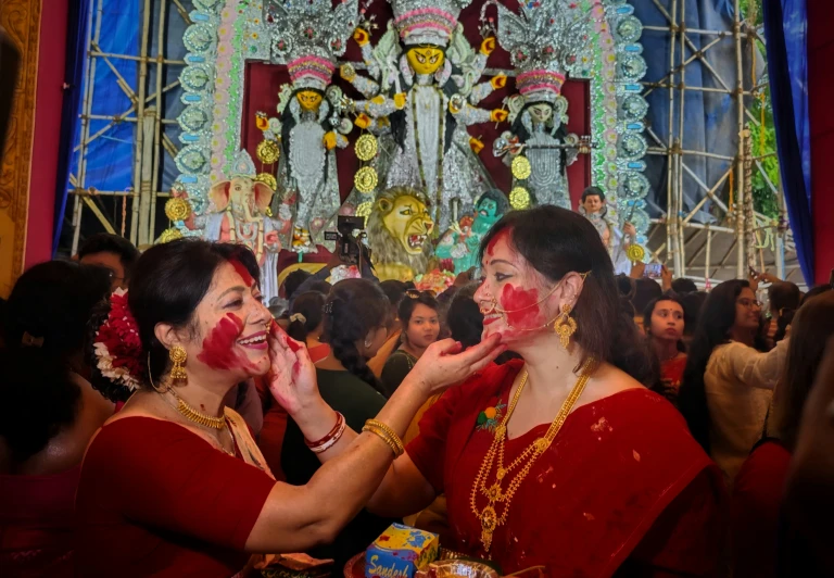 two women in indian attire are applying their faces with red paint