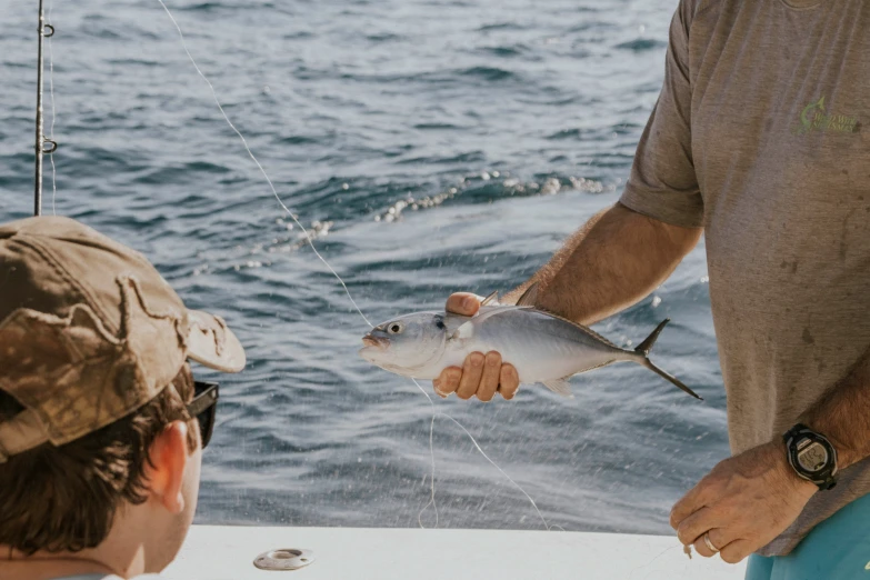 a man holding onto a fish from a boat while another man looks on
