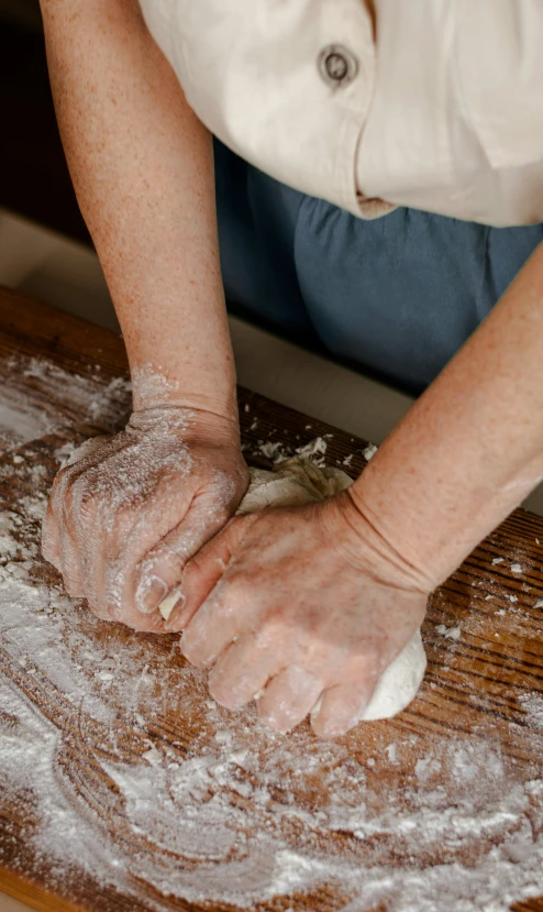 a woman holding a large knickzle of dough