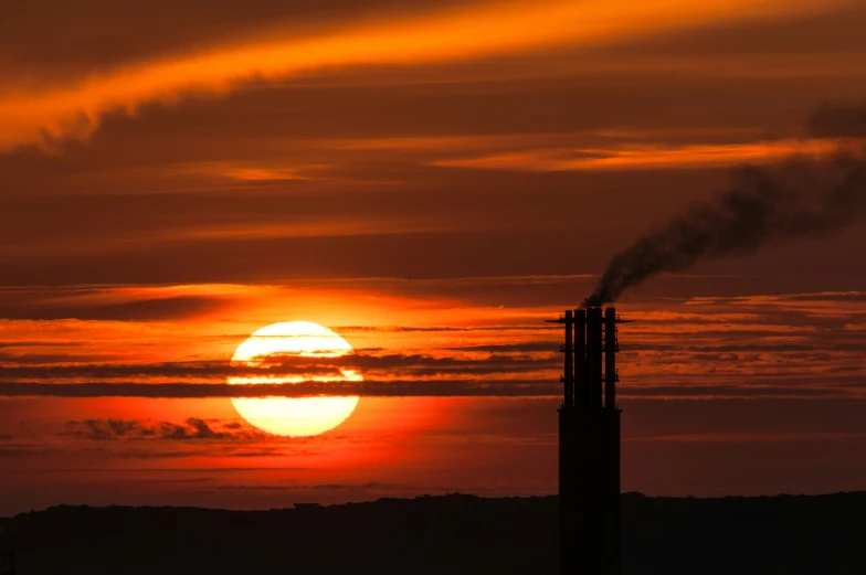 the sun rises behind an industrial pipe emitting smoke into the sky
