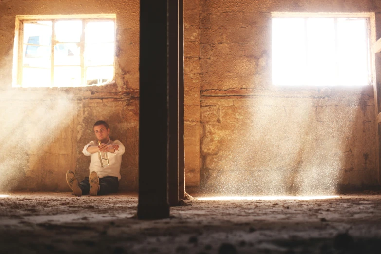 a man kneeling in a room next to two windows