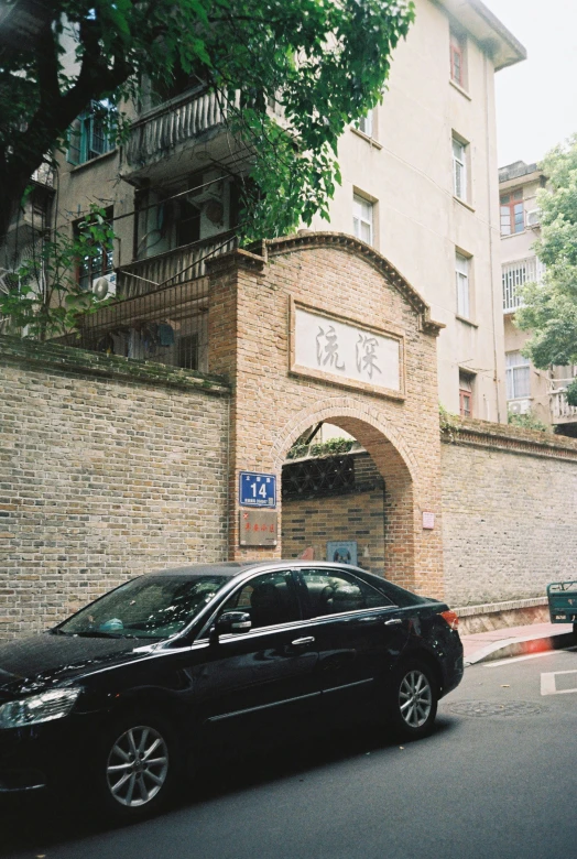 a black car parked by a building near a tall brick wall