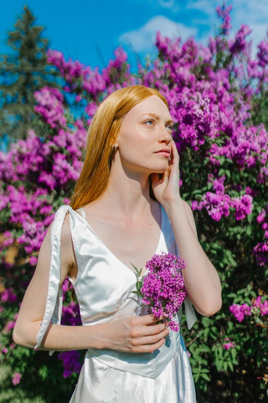 a beautiful woman standing next to purple flowers