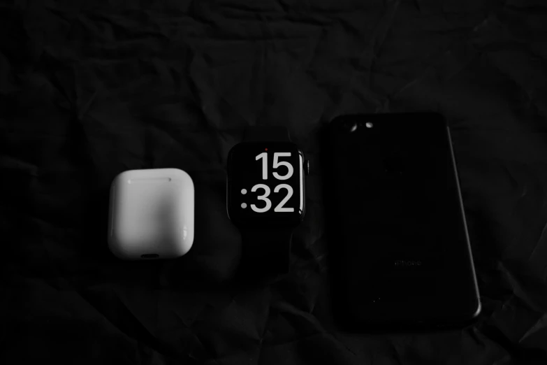 a clock, a smartphone and another electronics laying on the bed