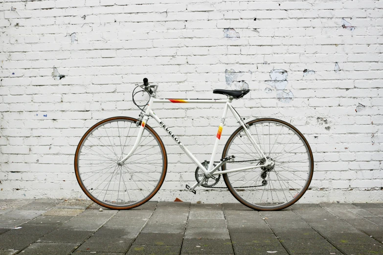 a white bicycle stands on pavement against a brick wall