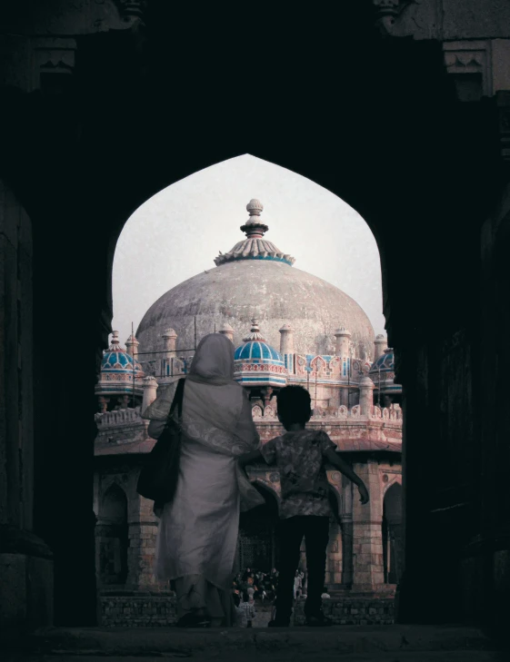 two people walking towards a domed building with a blue umbrella