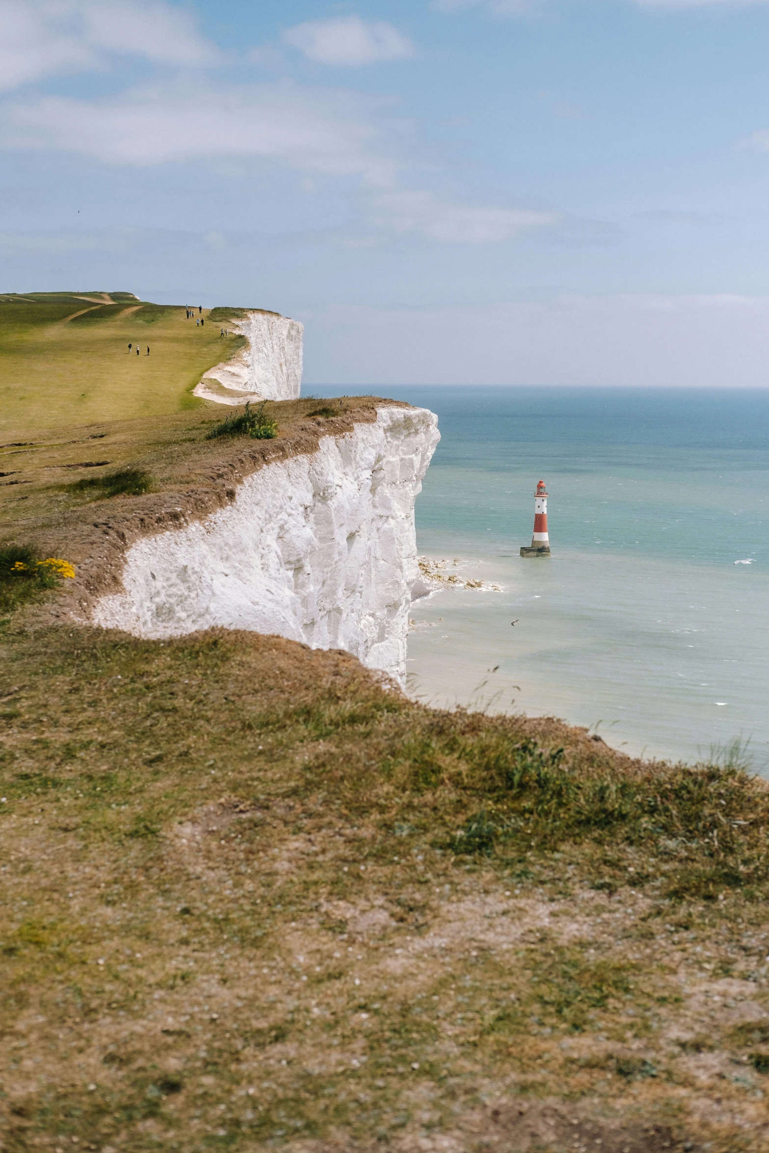 a white lighthouse standing on the top of a mountain near water