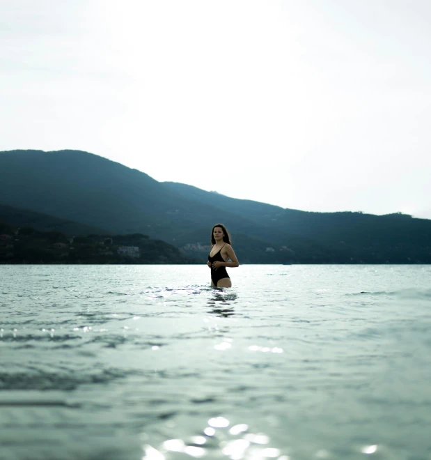 a woman with long hair and black panties walks in water near mountains