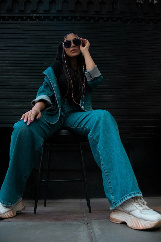 a woman in a jean pants and high - top sneakers sits on a chair and wears sunglasses