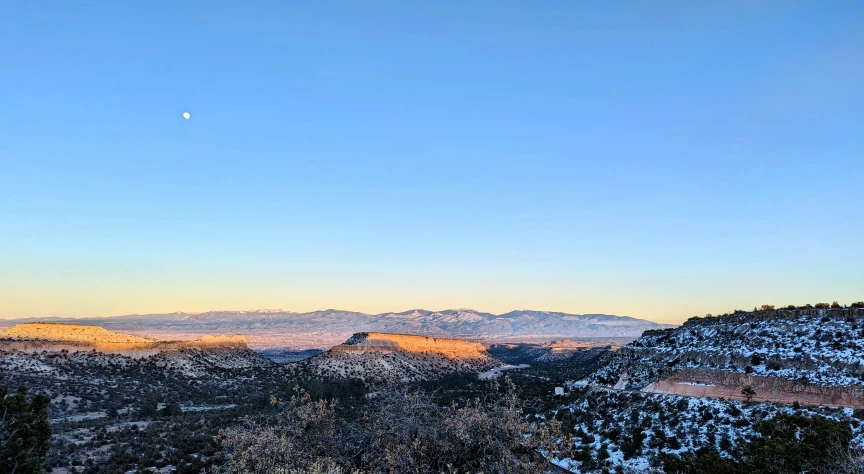 a hillside with snow covered trees and hills under a clear blue sky