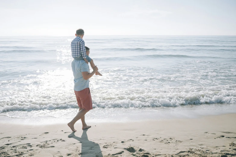 a man is holding a small child over his shoulders as he walks on the beach