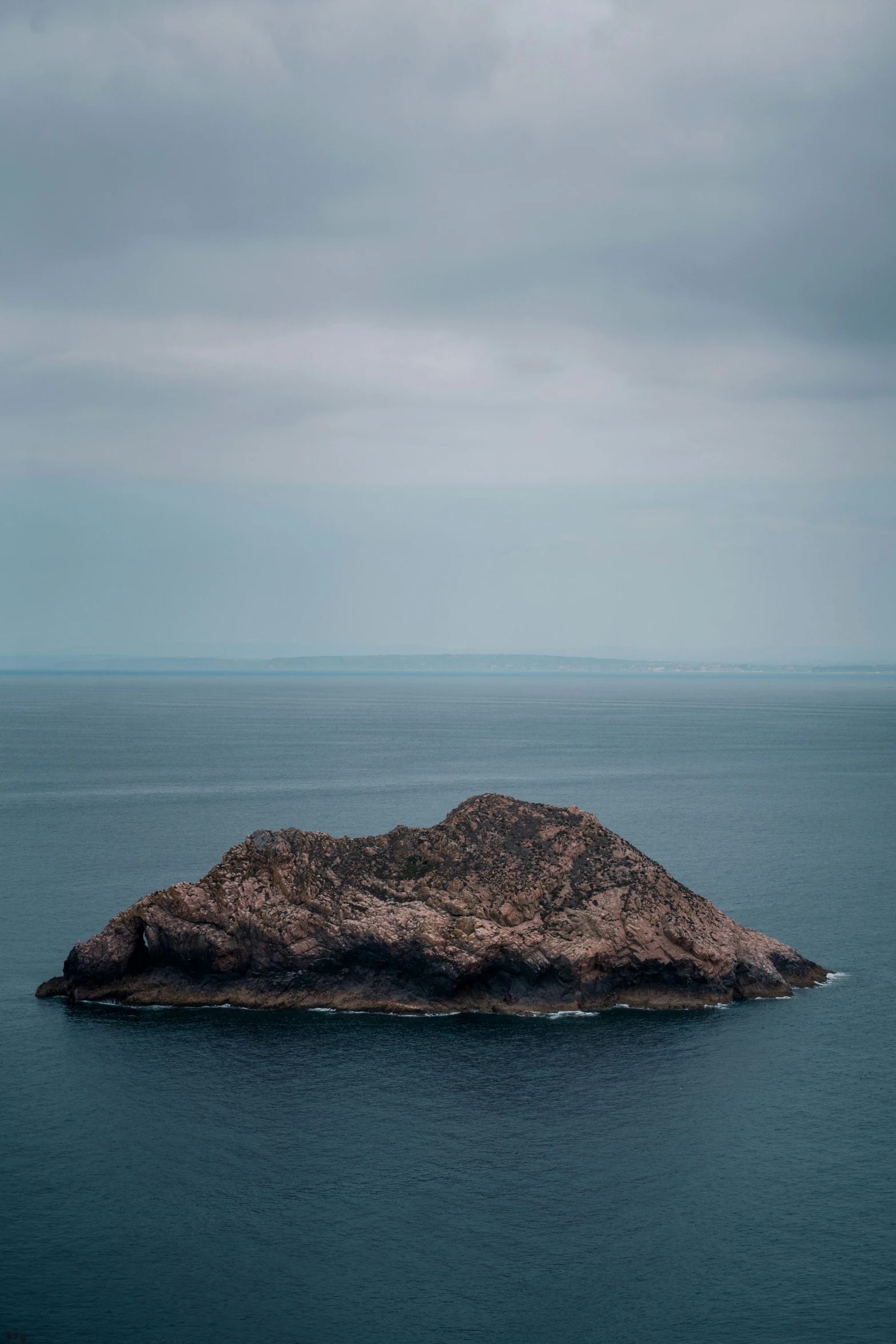 the rock is sticking out from the ocean in front of a cloudy sky