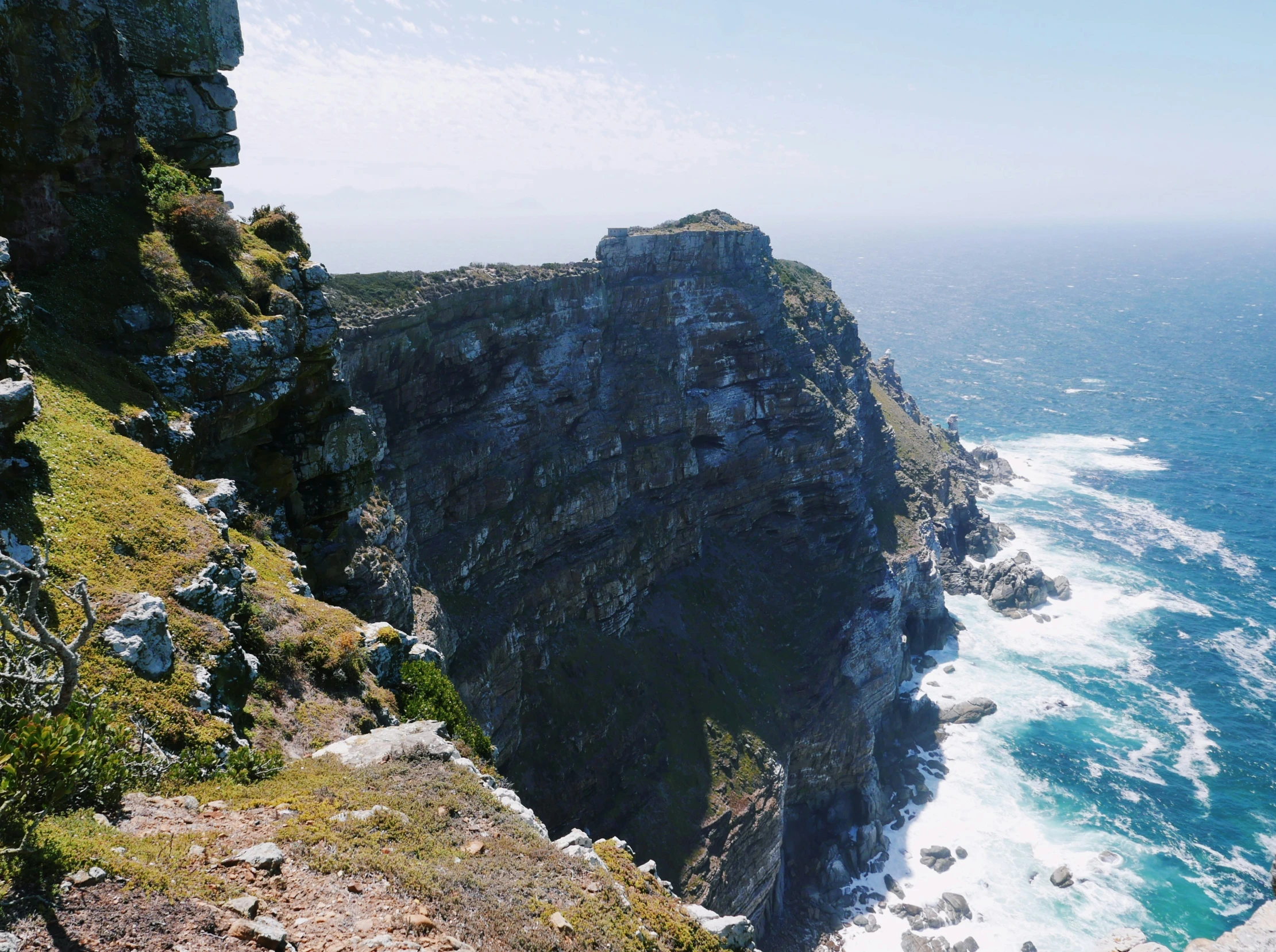 the cliff next to the ocean has a green grass patch on top of it