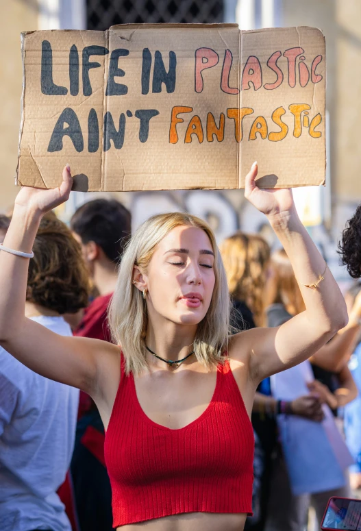 a young woman holding a sign reading, life in plastic, don't fantastic