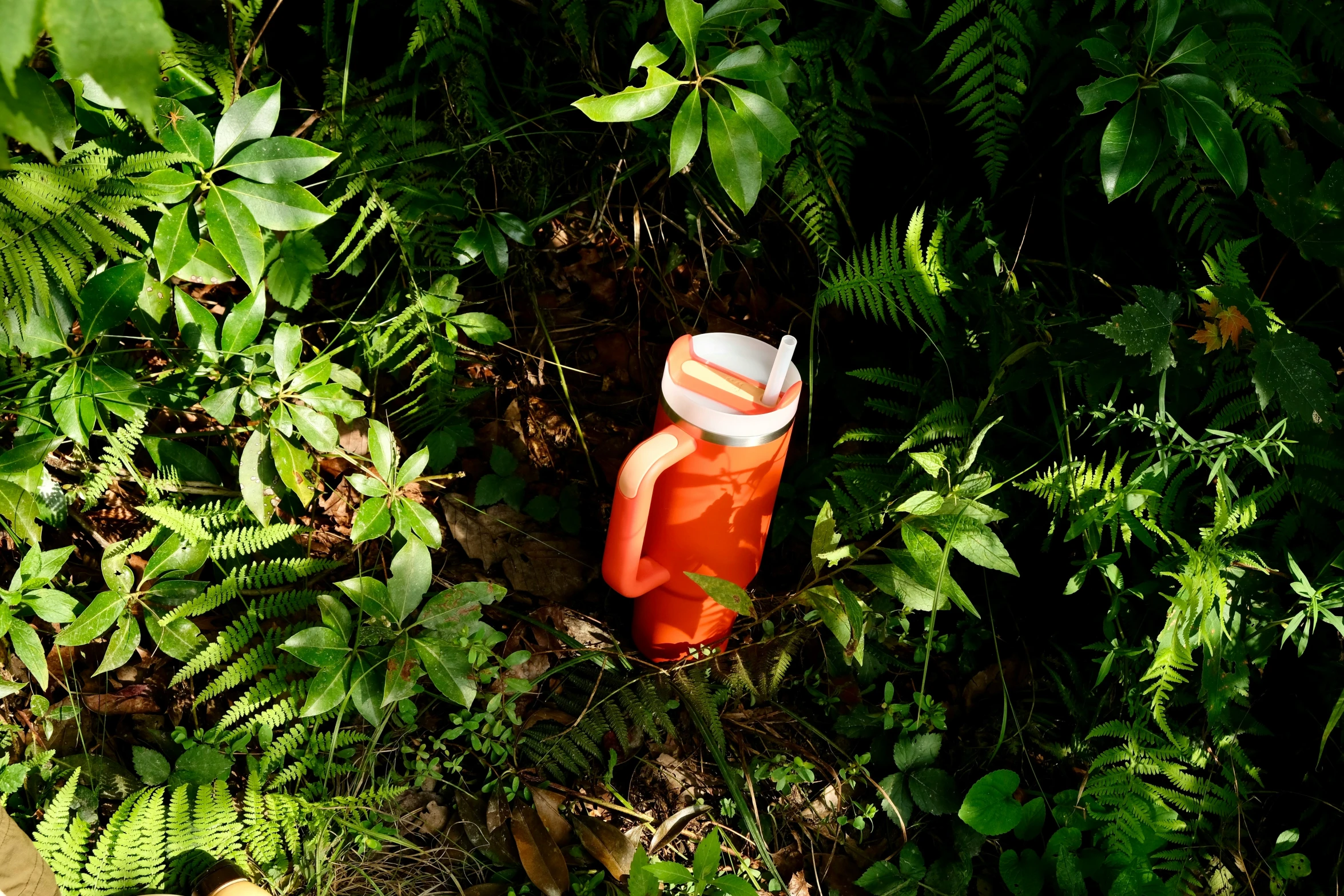 an orange plastic water bottle is standing on the grass