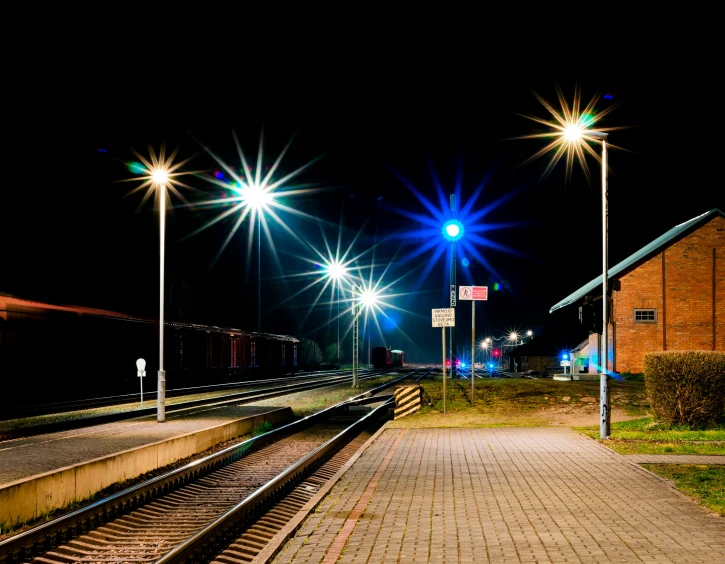 a sidewalk next to train tracks with lots of lights