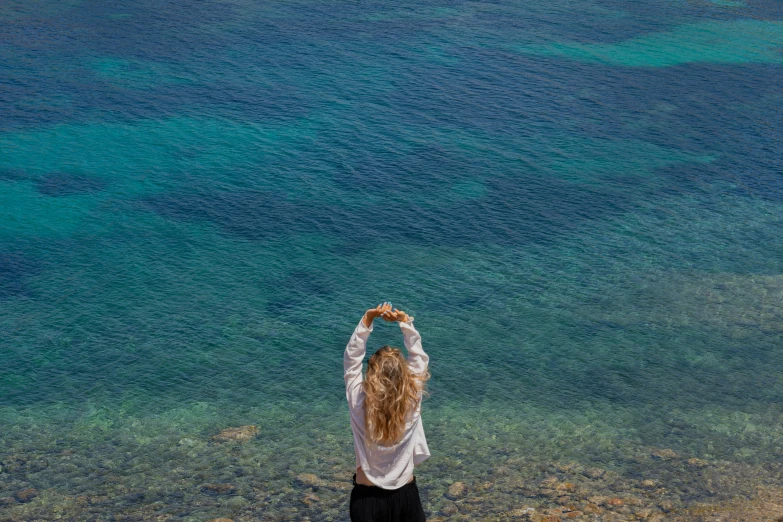 woman standing in front of the ocean and reaching up to see the water